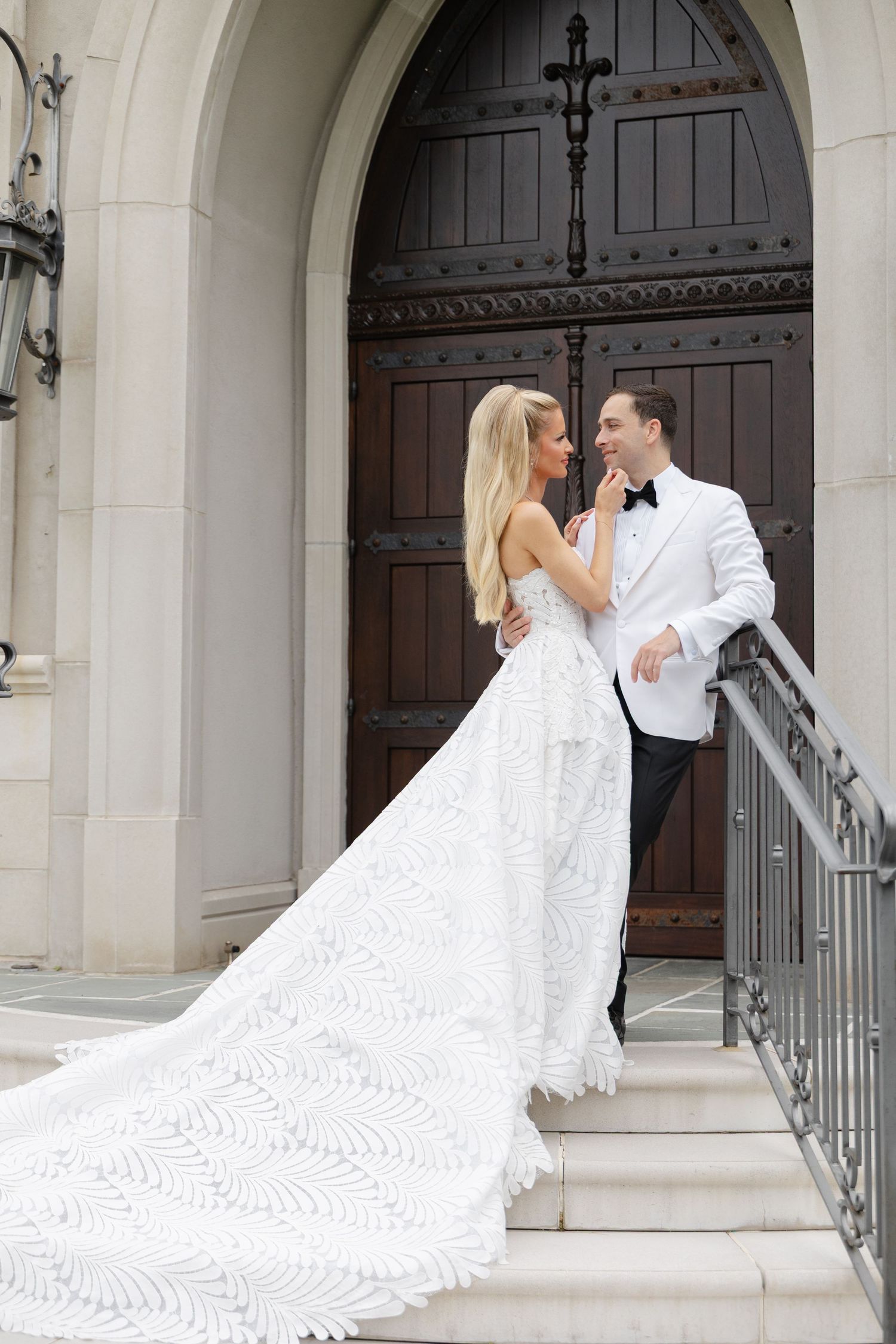 A romantic wedding couple shares intimate moments in front of a grand church entrance with ornate wooden doors.