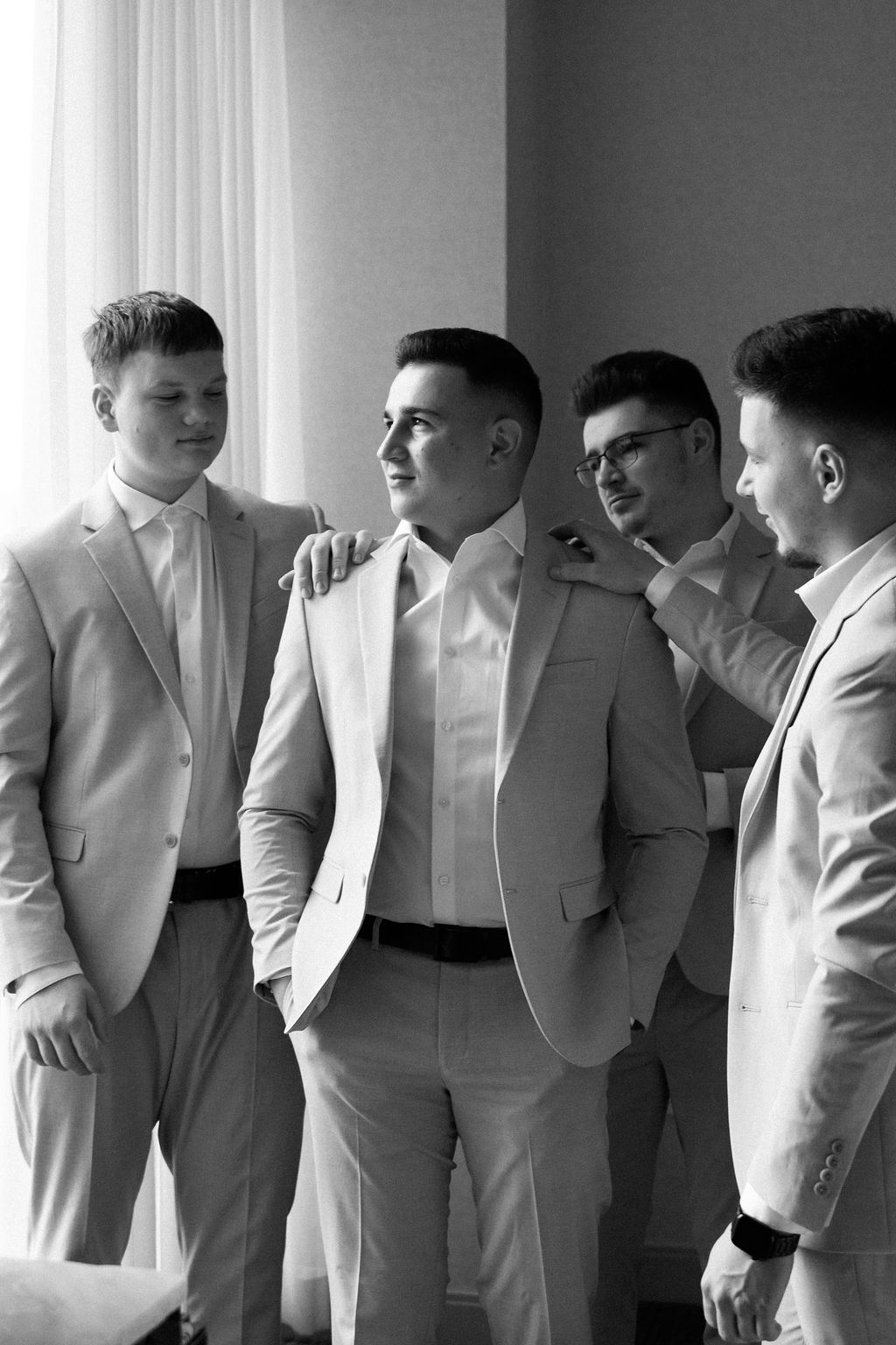 Groomsmen in light colored suits stand in a row against a wall creating an elegant wedding party portrait.