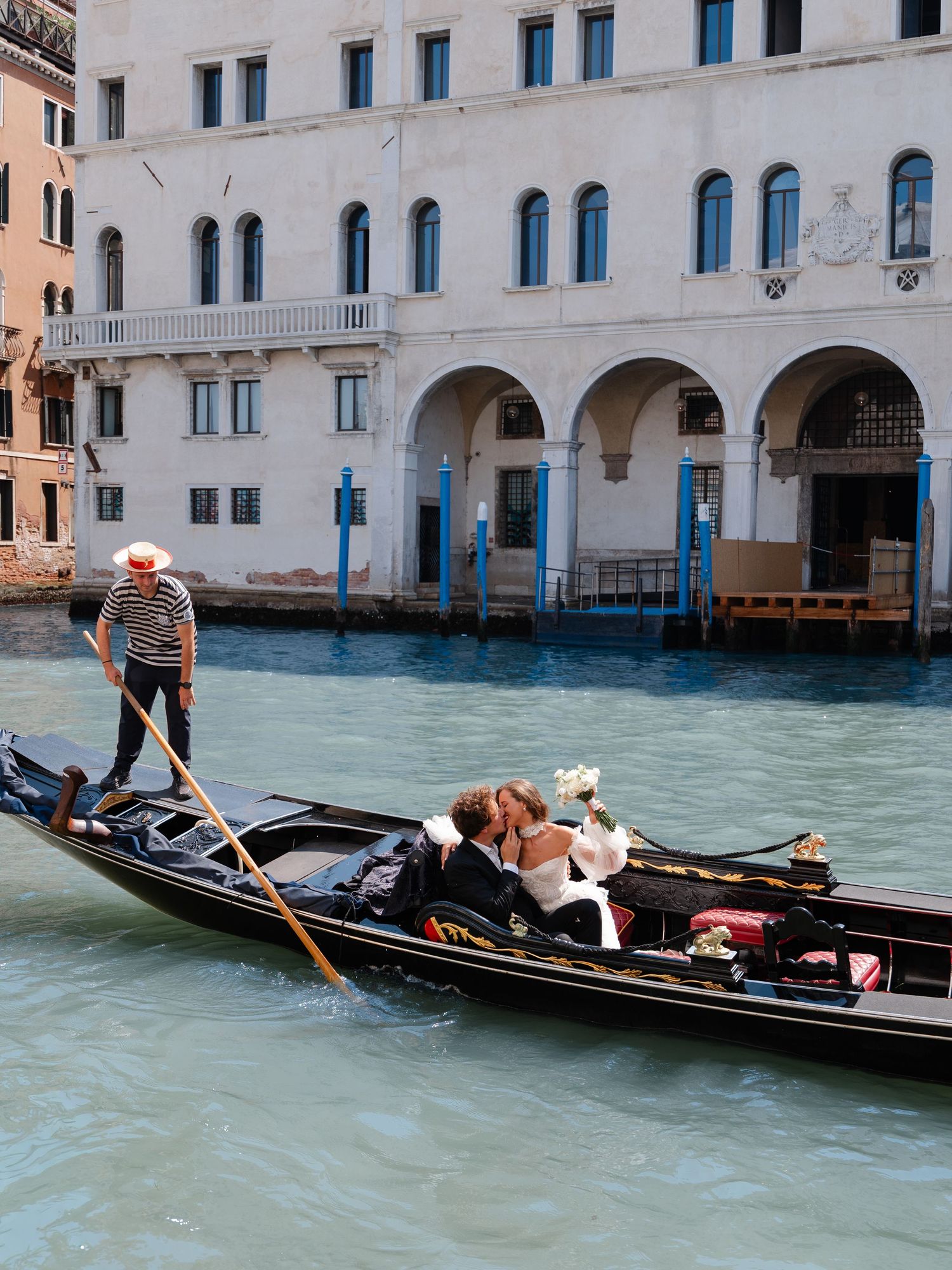 A traditional black gondola glides through the turquoise waters of Venice's canals past historic white stone buildings.