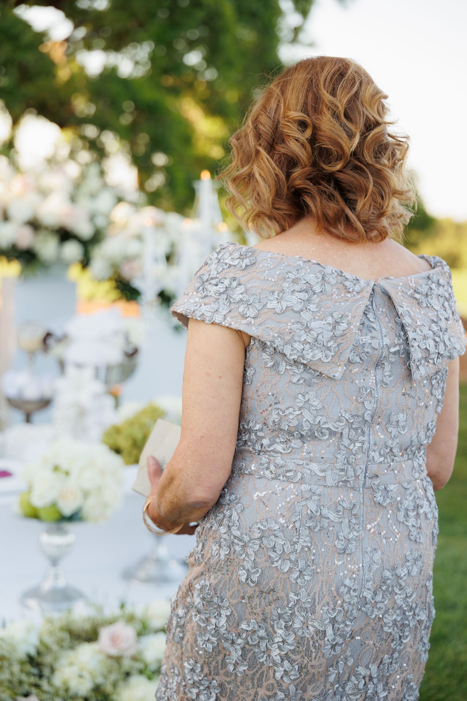 Close-up view of a silver-gray lace dress with delicate floral embellishments and cap sleeves against a garden backdrop.