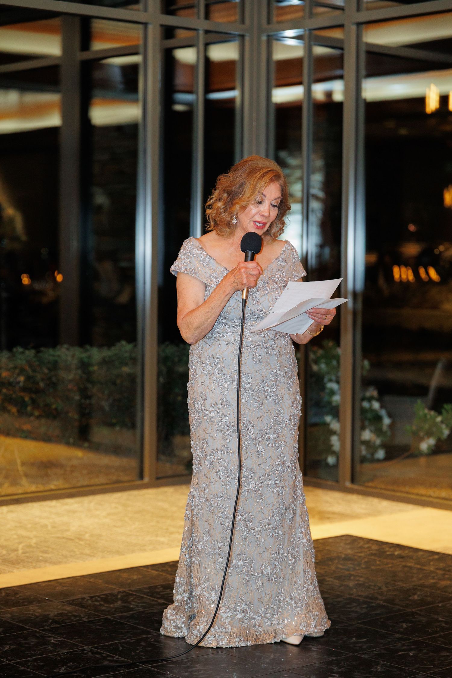 A person in a sparkly silver dress gives an emotional speech at a podium during an evening event.