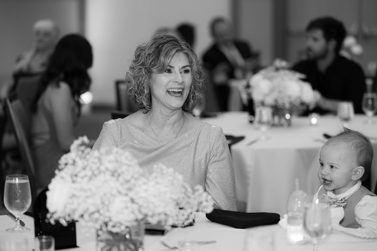 Black and white candid photo of guests laughing and socializing at a formal reception event.