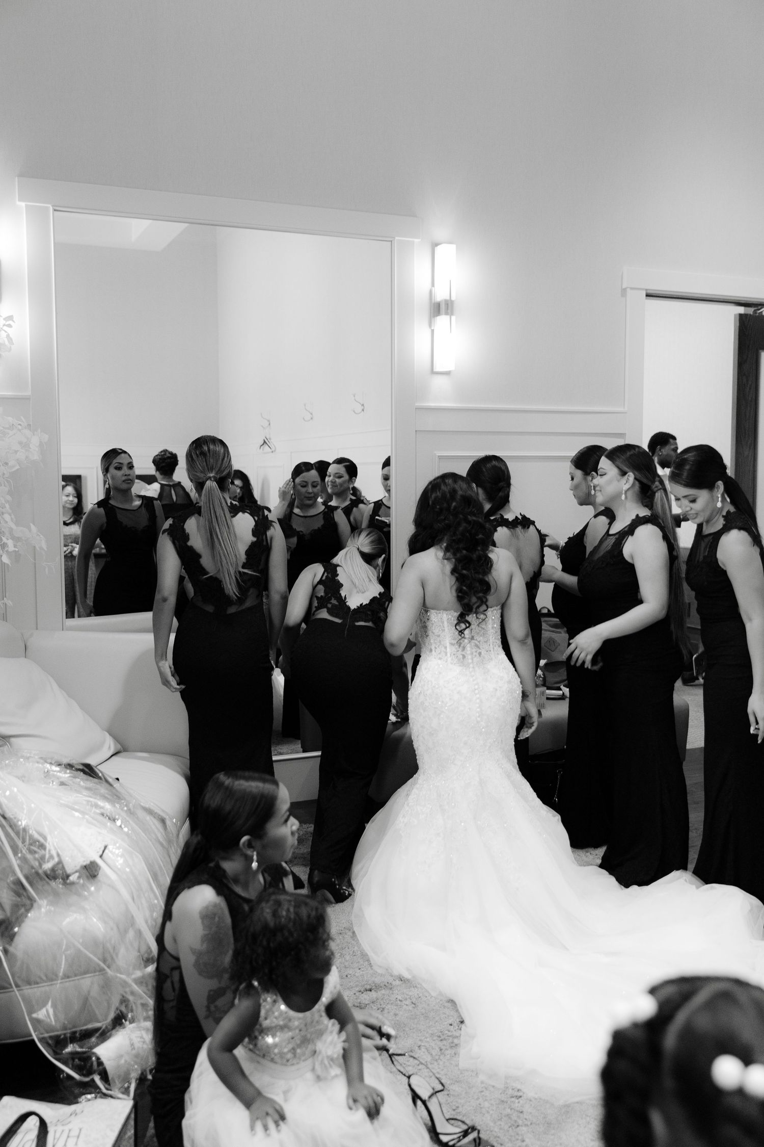 A group of wedding guests and a bride in a white gown gather in what appears to be a reception venue hallway.