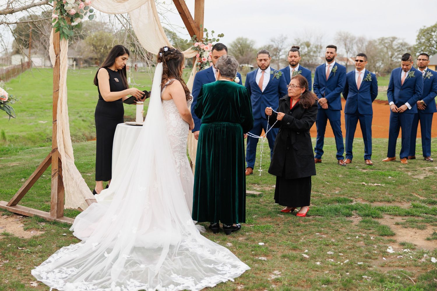 Wedding party in navy suits and dark green dresses poses outdoors on a grassy lawn during autumn celebration.
