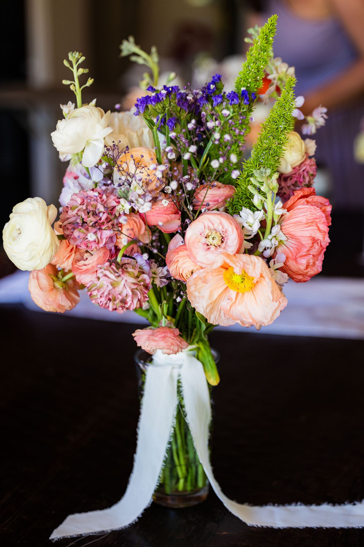 Elegant wedding floral centerpieces with coral peonies and white blooms arranged in glass vases with delicate ribbon accents.