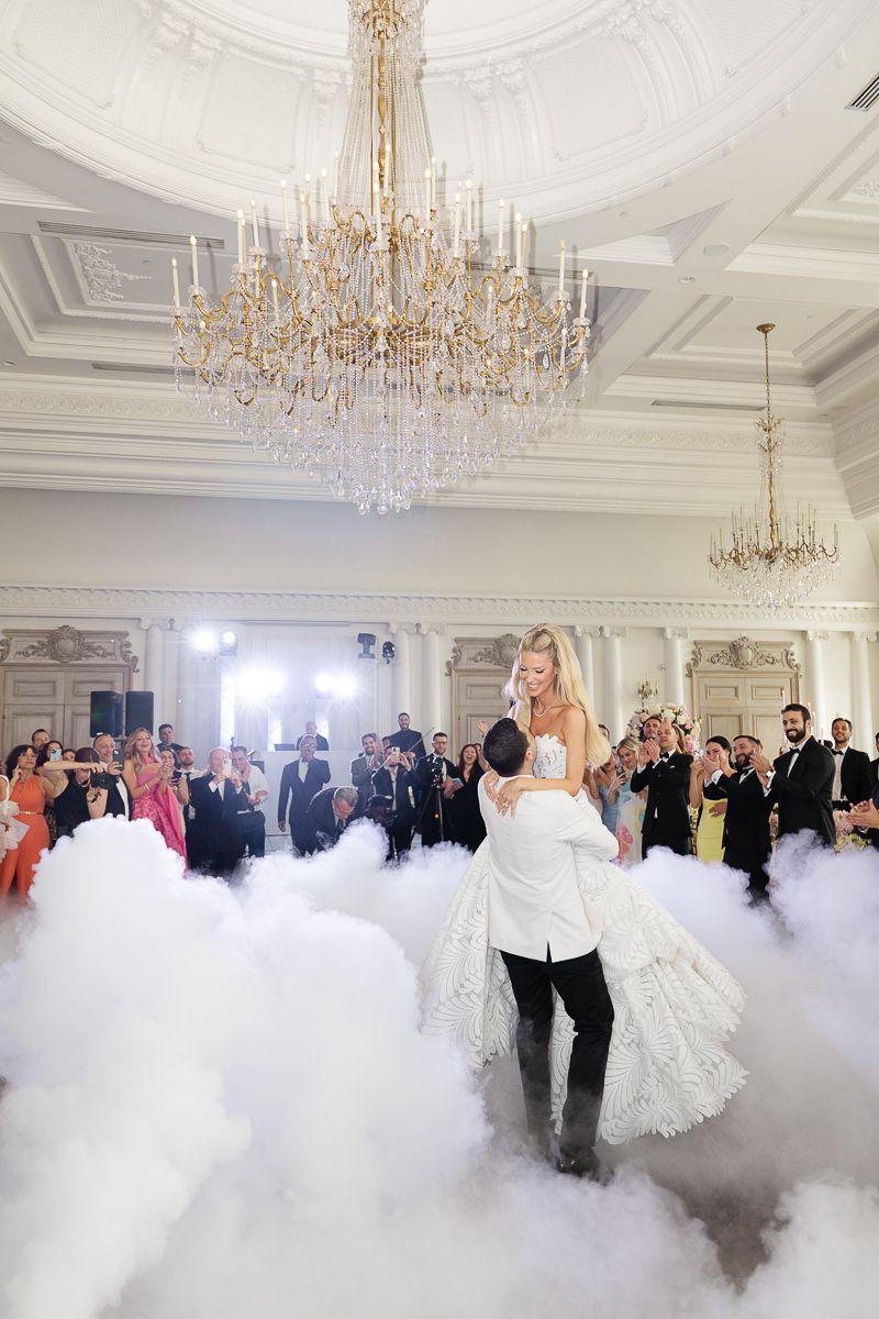 A romantic first dance in an elegant ballroom with crystal chandeliers and dramatic fog effects.
