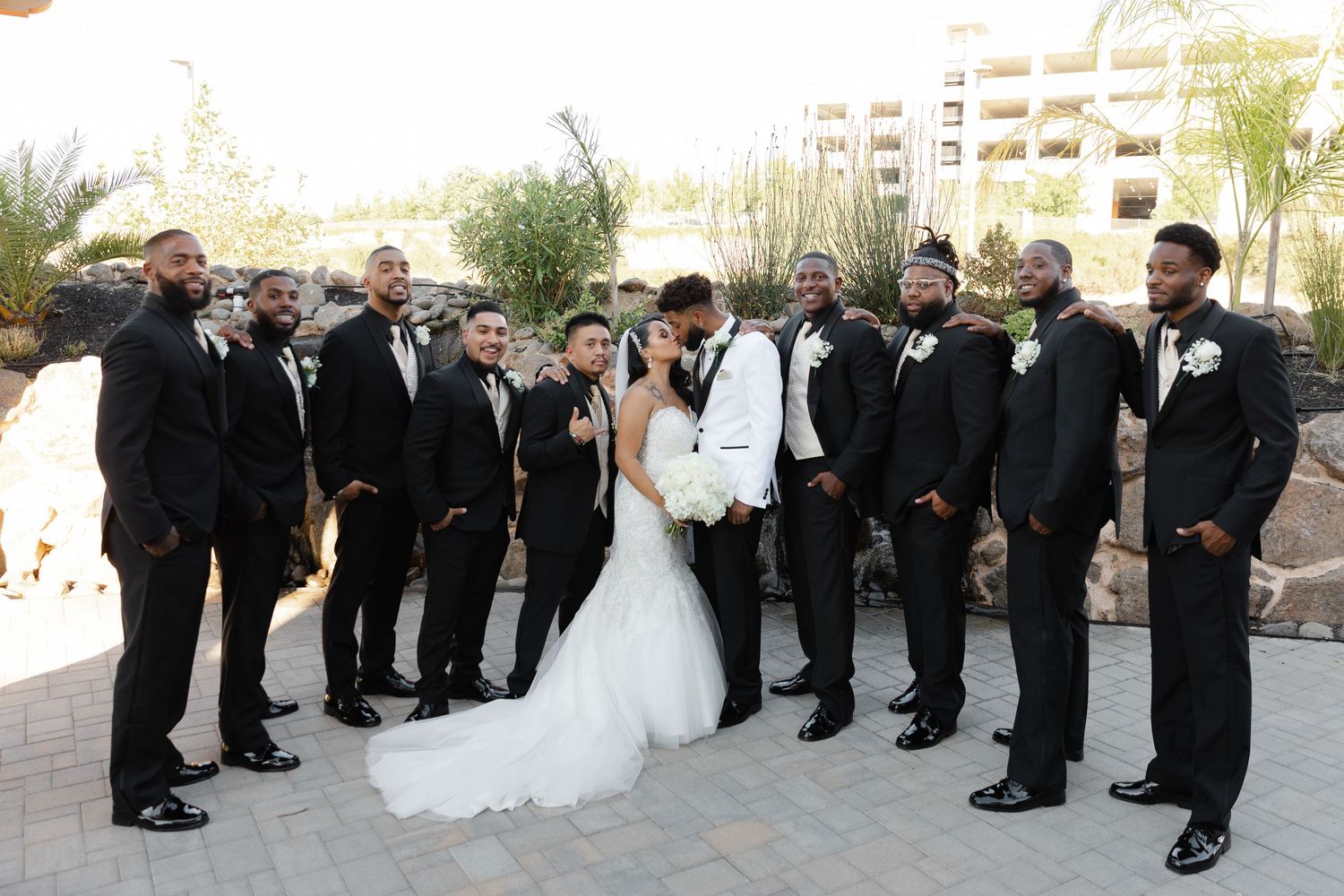 Wedding party in formal black and white attire lined up outdoors for a group photo at an elegant venue.