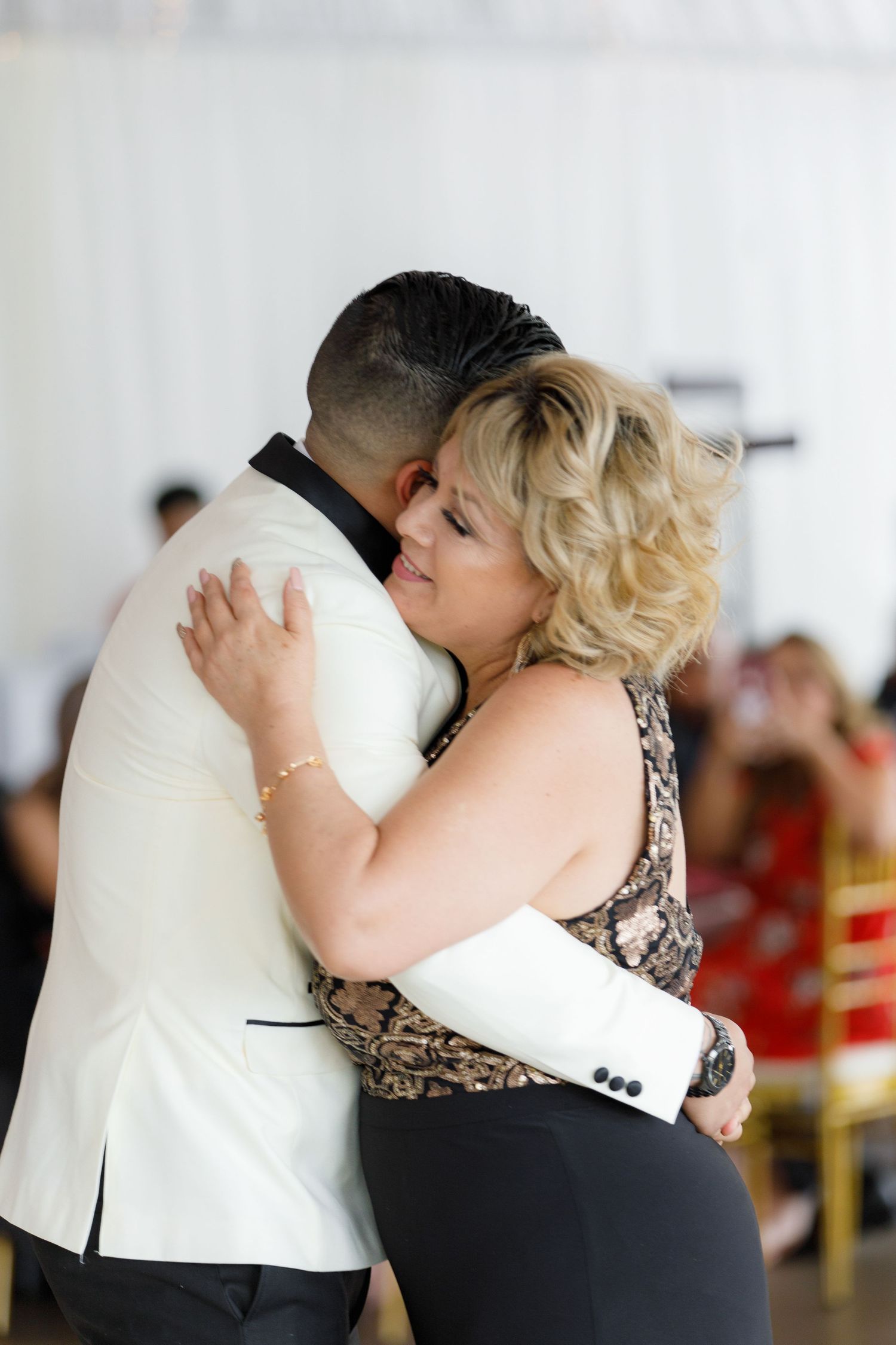 A sequence of four photos showing an emotional embrace between two people at what appears to be a formal event.