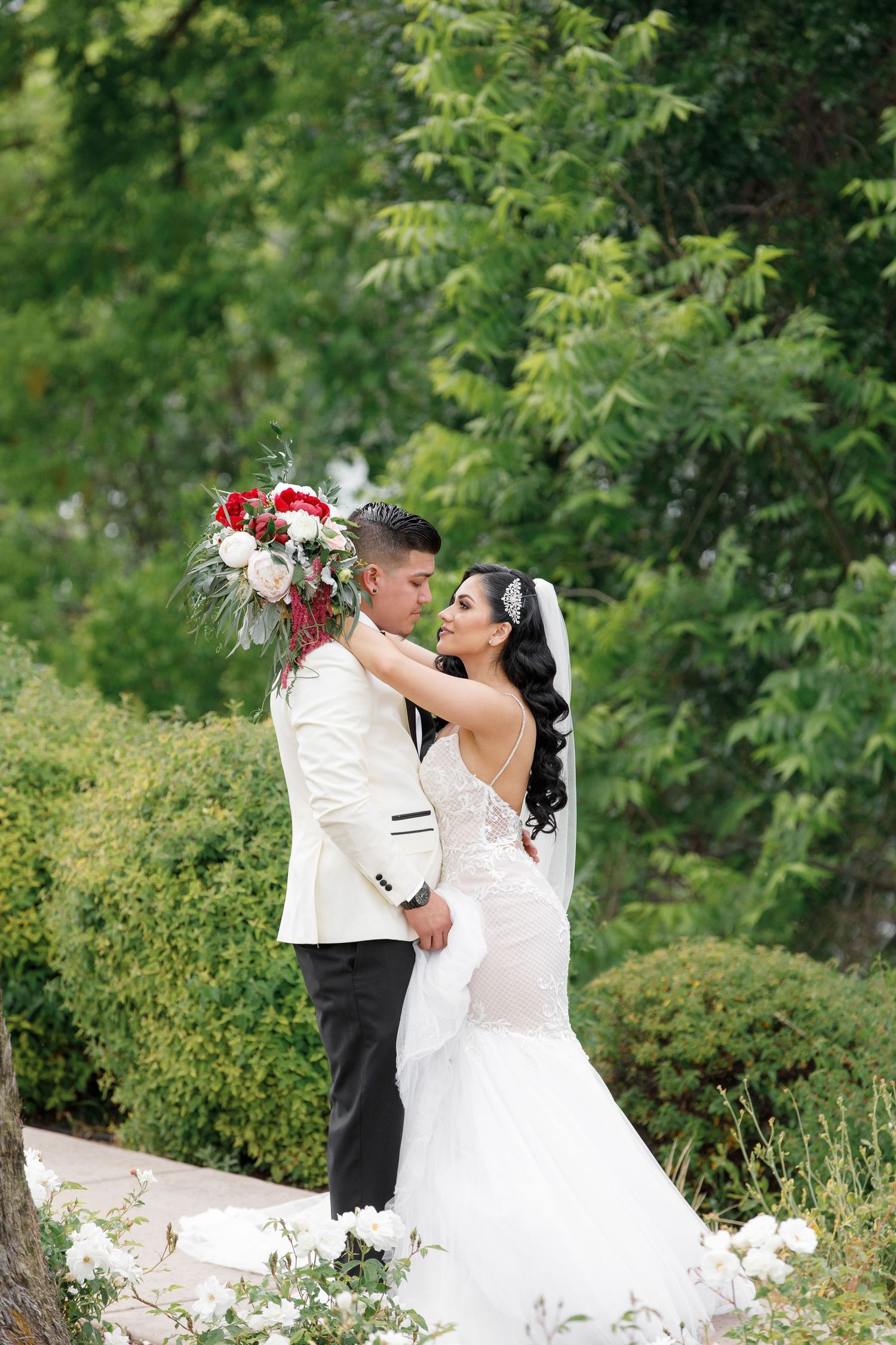 A couple in wedding attire share romantic moments in a lush garden setting during their outdoor photo session.