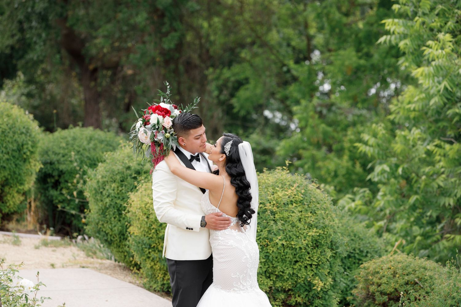A romantic outdoor wedding photoshoot in a lush green garden setting with a white bridal gown.