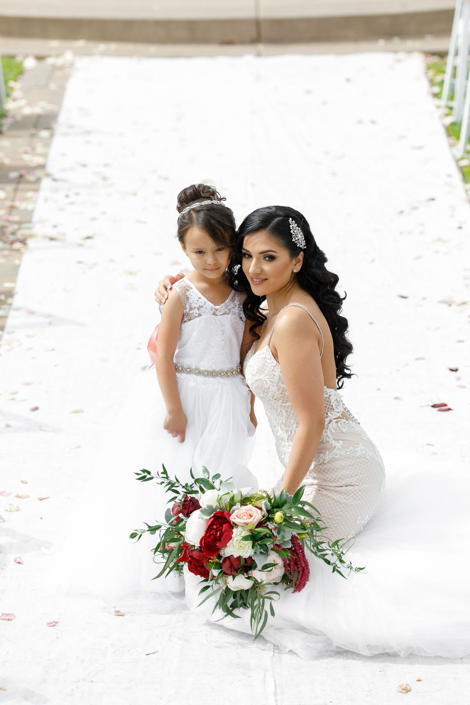 Two people in white wedding dresses share an intimate moment on a sandy beach surrounded by rose petals.