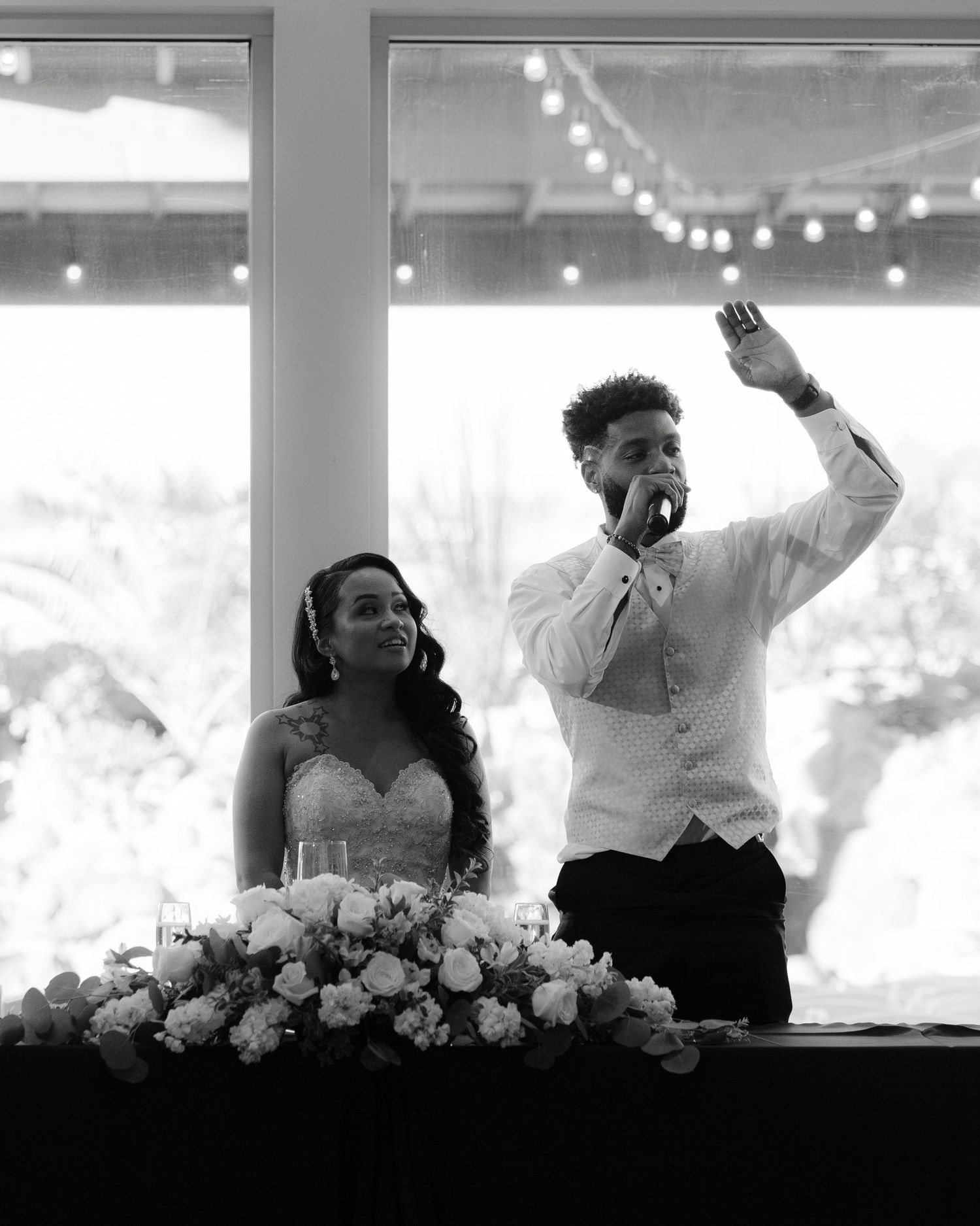 A series of black and white candid reception photos showing a couple celebrating at their wedding table with joyful gestures.