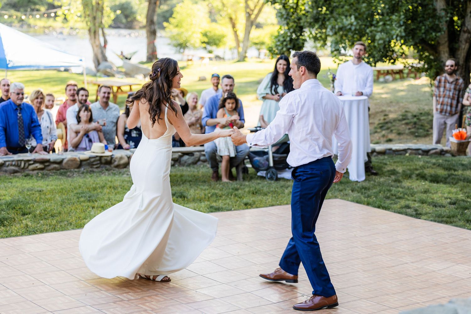Wedding guests watch as dancers perform on an outdoor patio during a sunny afternoon celebration.