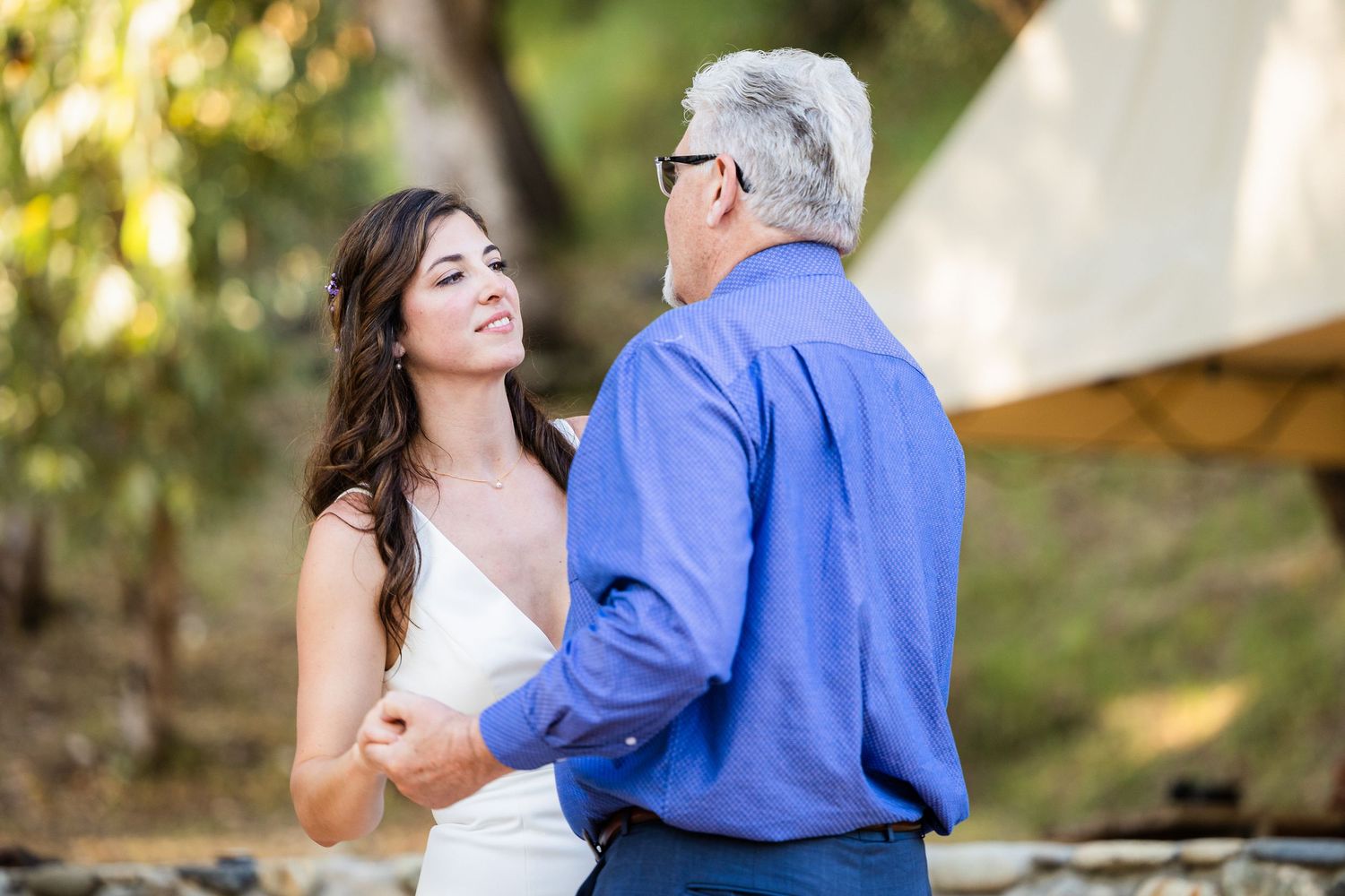 A couple shares a tender moment together during an outdoor wedding photoshoot in a sunlit garden setting.