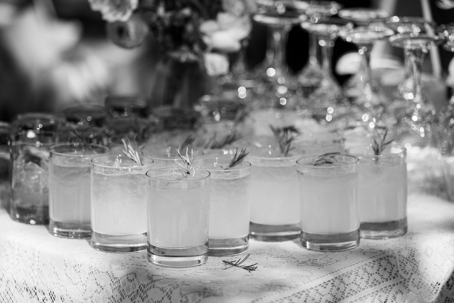 Rows of elegant cocktail glasses filled with white drinks garnished with herbs on a decorated table at an event.