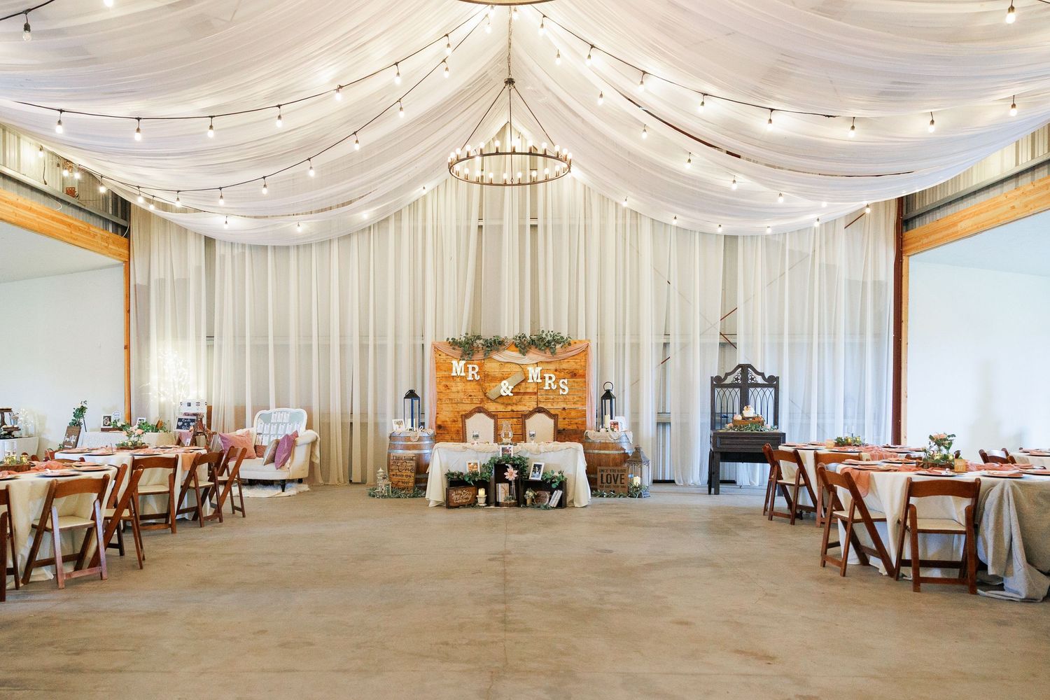 White fabric drapes elegantly from the ceiling of an elegant wedding reception venue with string lights and wooden tables.