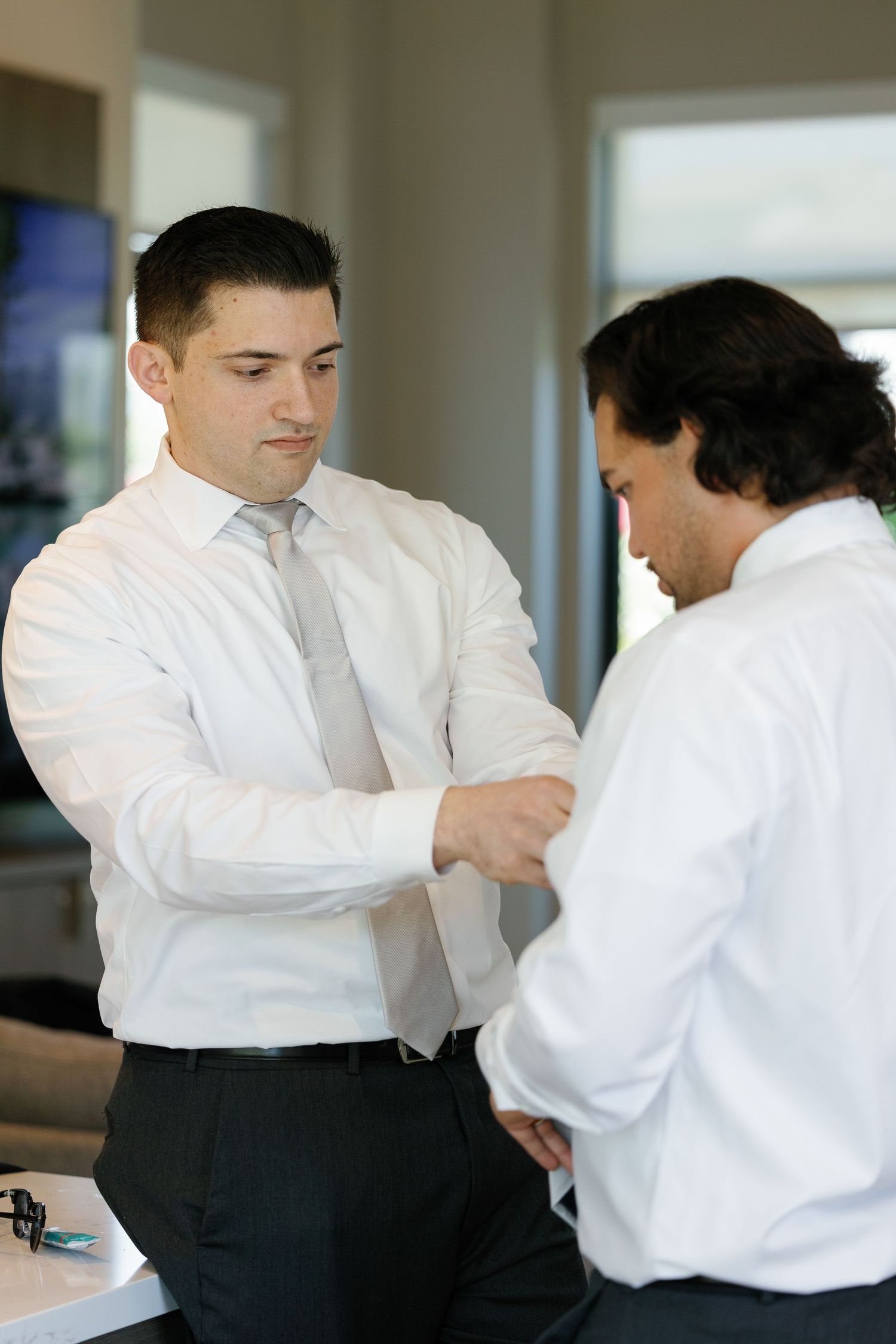 Two martial artists in white shirts and black pants practice self-defense techniques in a bright studio space.