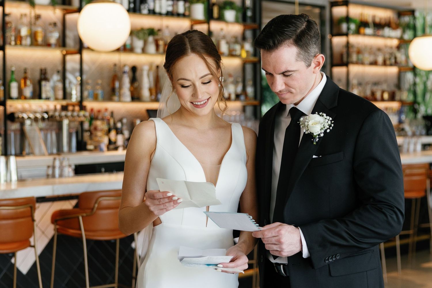 Couple in formal wedding attire sharing a joyful moment while reading together at an elegant bar setting.