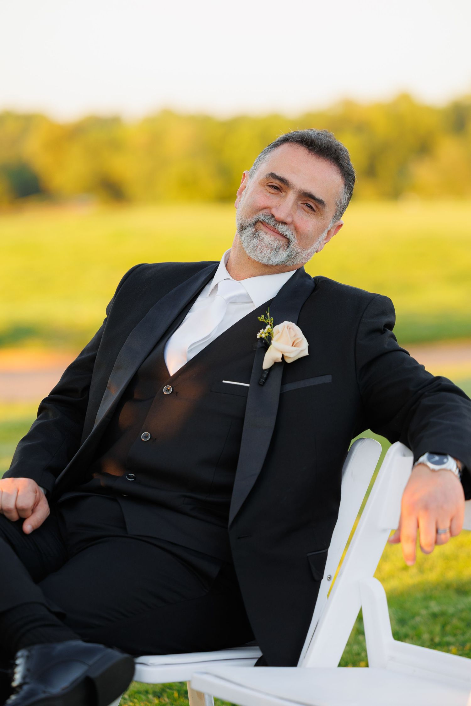 A person in a black suit rests peacefully in an outdoor Adirondack chair against a golden sunset backdrop.