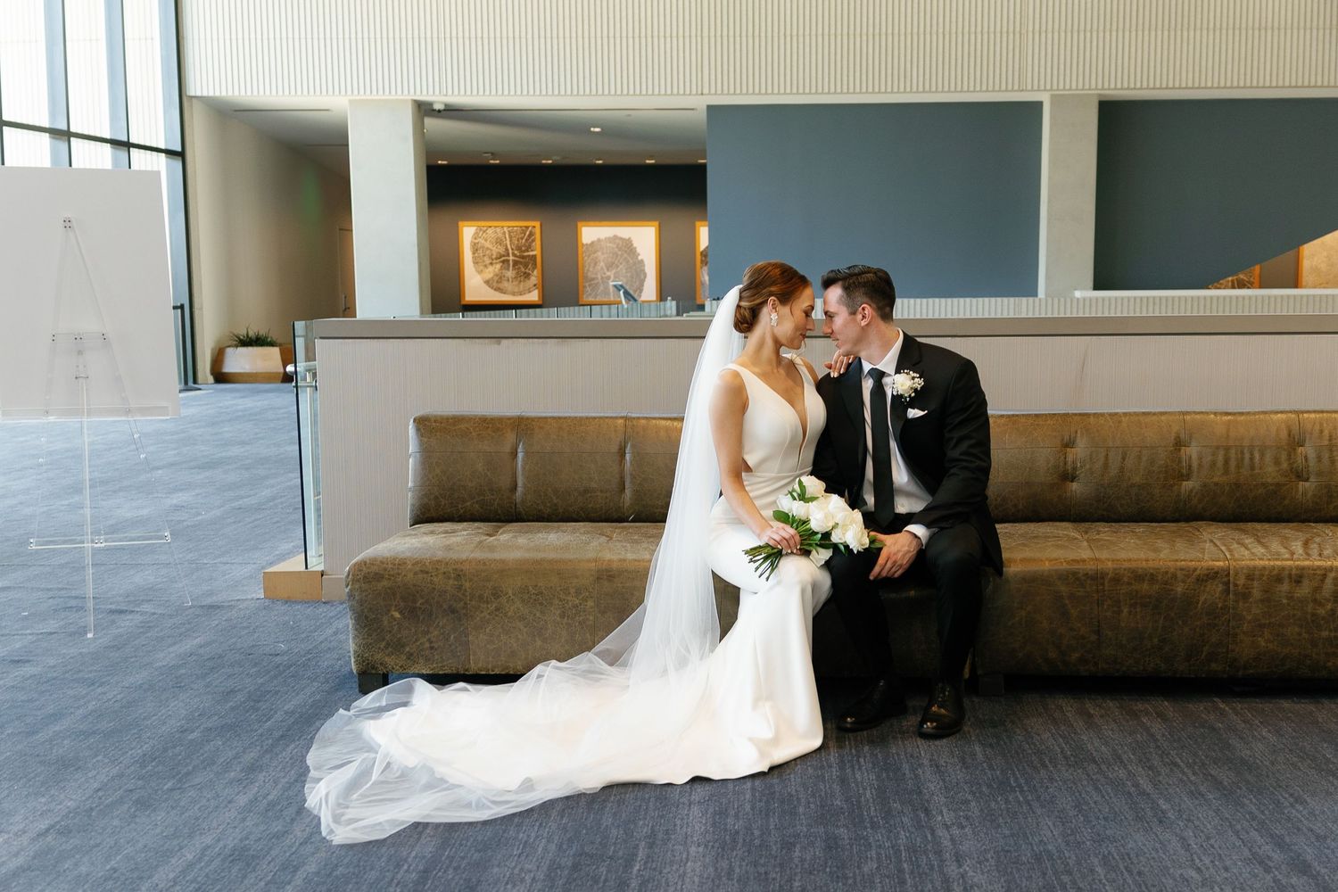 A wedding couple shares romantic moments in a modern architectural setting with concrete walls and natural lighting.