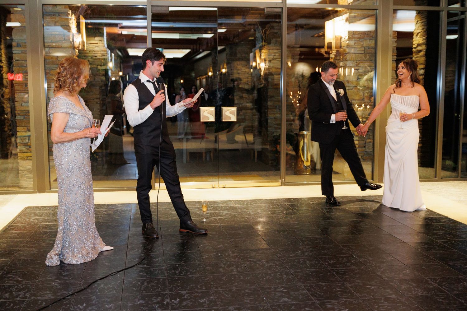Wedding party members strike playful poses in formal attire at an elegant venue entrance.