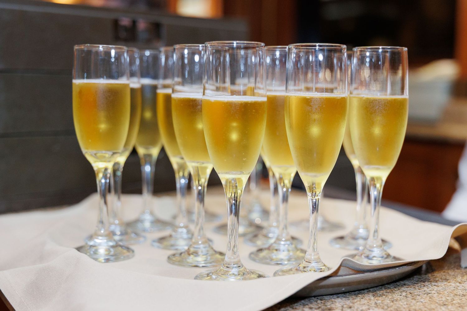 Rows of elegant champagne flutes filled with golden sparkling wine sit ready to be served at an event.