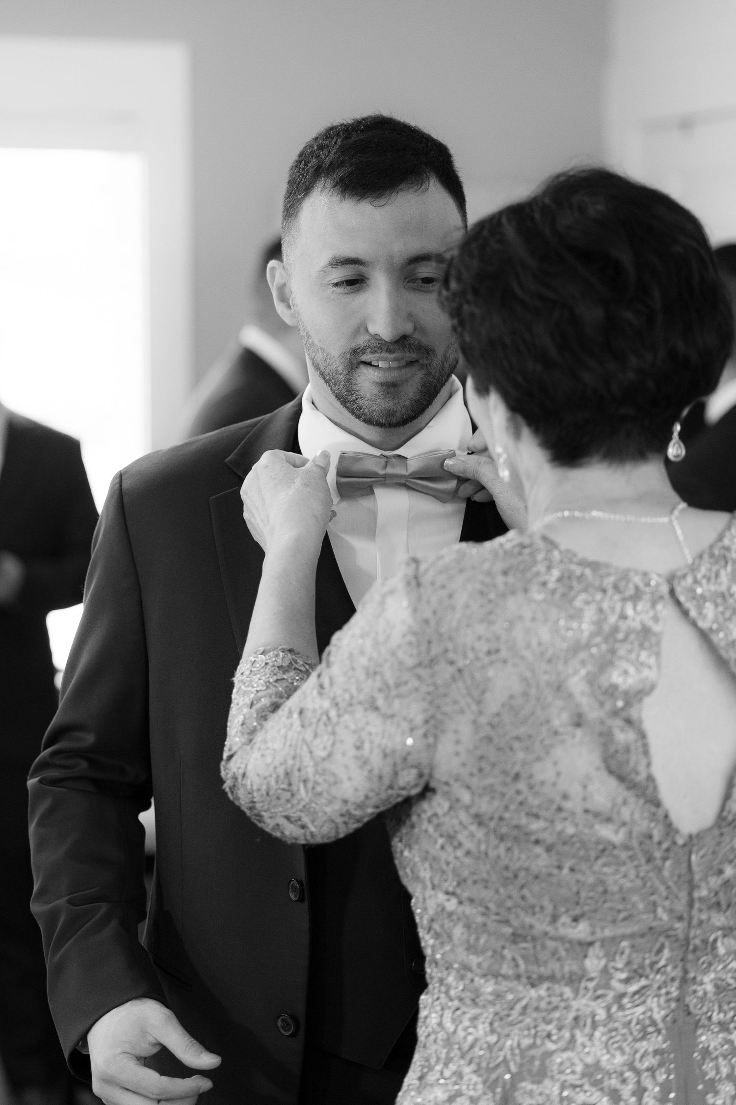 A tender black and white wedding moment as someone adjusts the groom's bowtie before the ceremony.