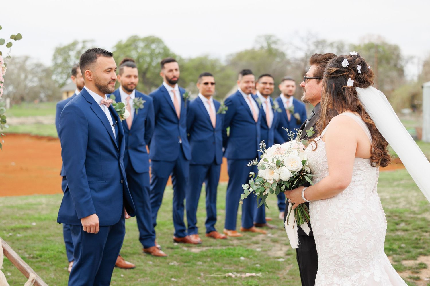 Wedding party wearing navy blue suits and white dress poses together in a scenic outdoor setting.