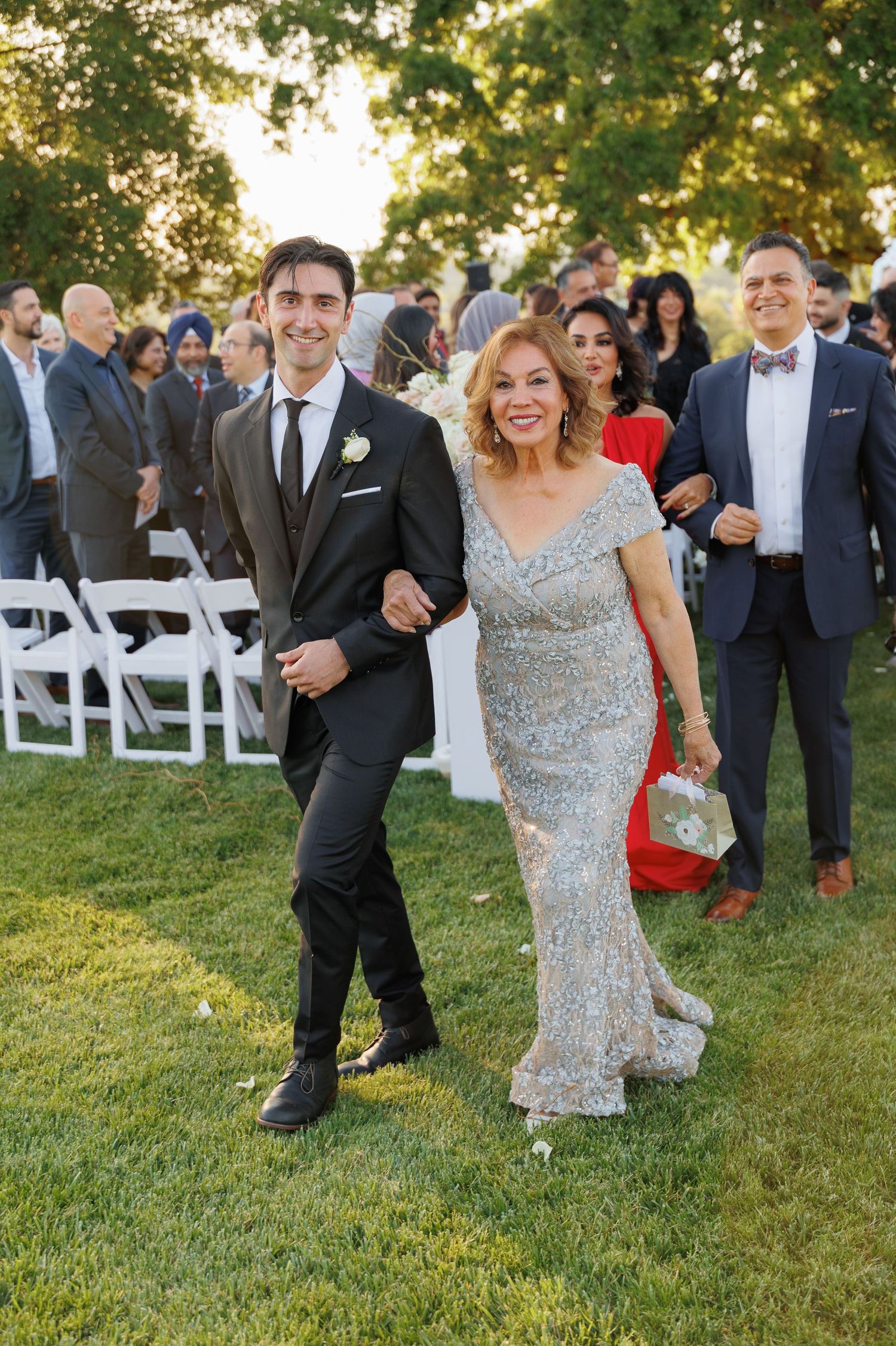 Wedding guests in formal attire gather on a sunny lawn during an outdoor ceremony reception.