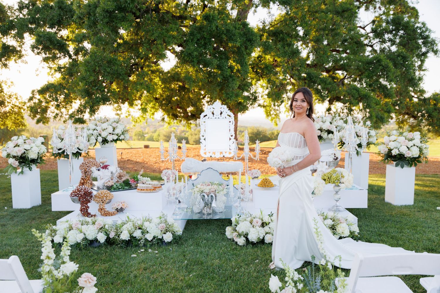 A beautiful outdoor wedding ceremony setup with white chairs and floral arrangements at sunset in a garden setting.
