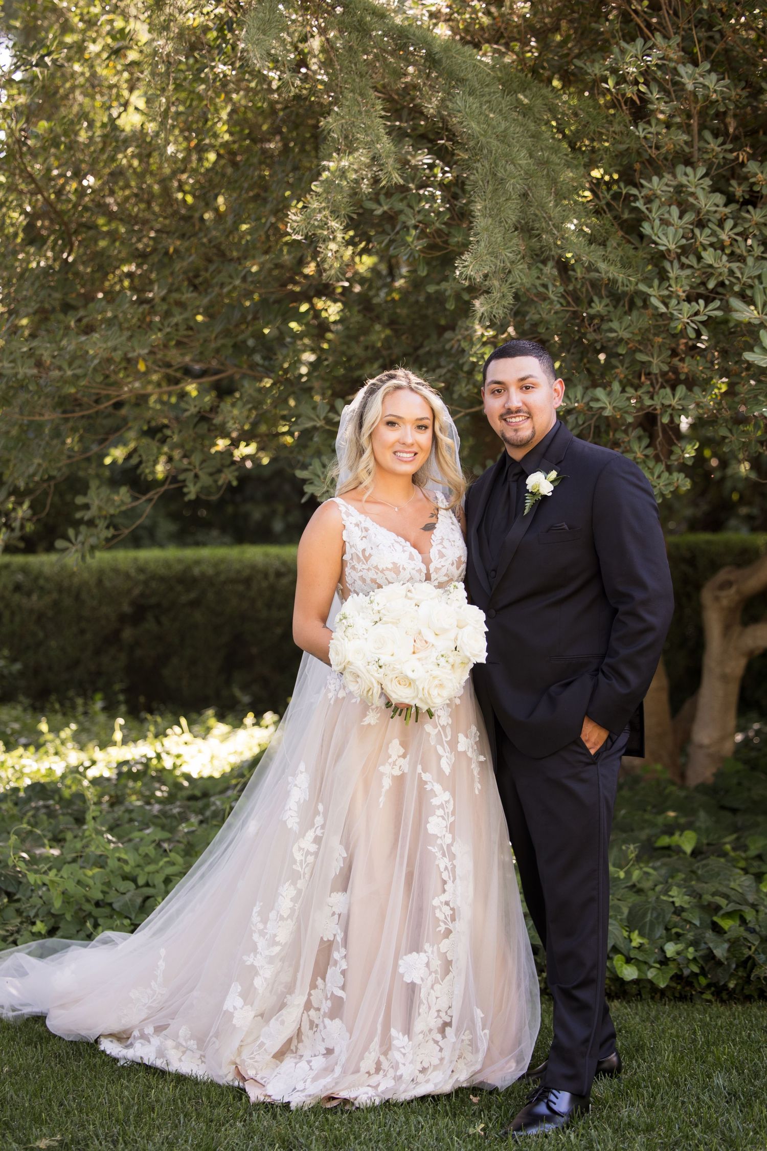 Garden wedding photoshoot with elegant lace gown and formal attire among blooming trees.