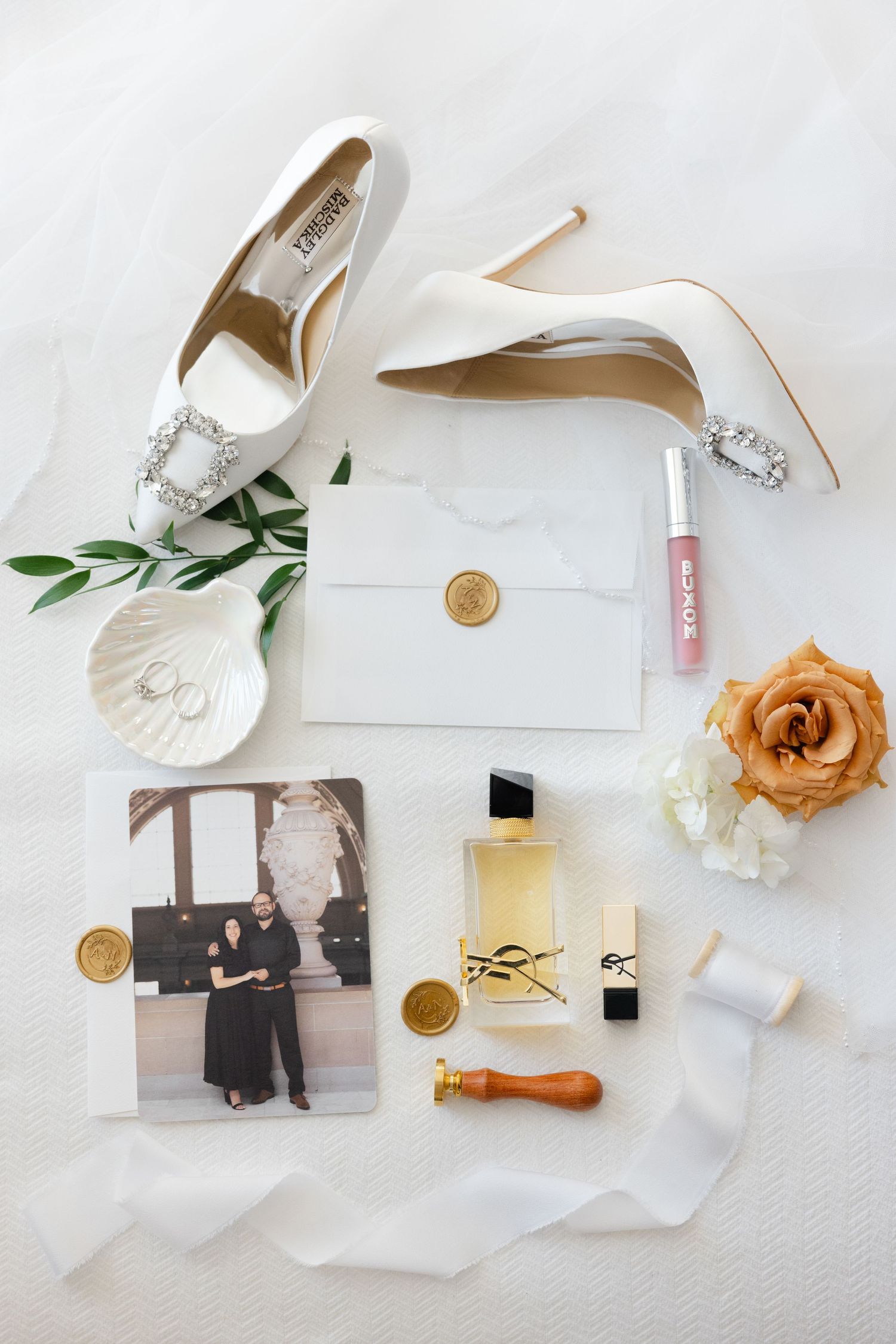 Wedding details flatlay with elegant white shoes, rings, flowers and photographs on light fabric.