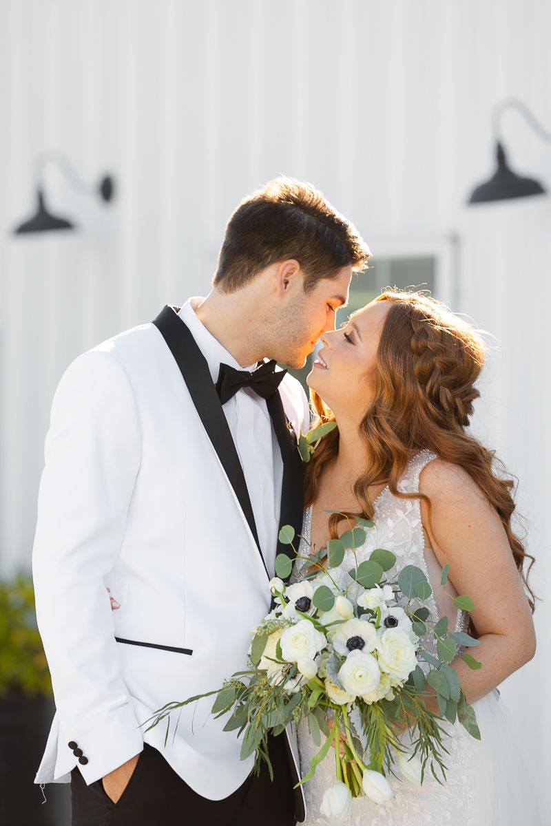 A romantic wedding portrait features a couple in white attire sharing an intimate moment with a white bouquet.