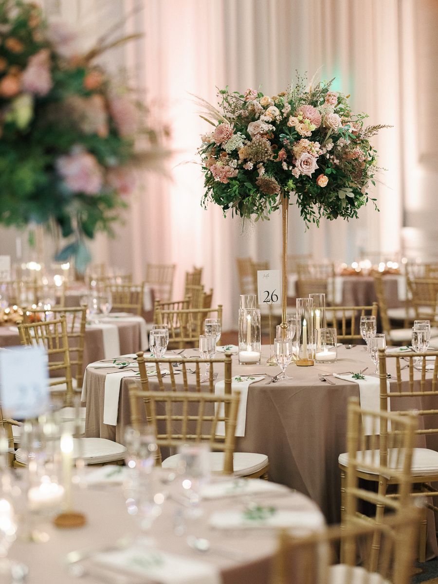 Elegant wedding reception tables with gold chairs, floral centerpieces, and soft lighting in a luxurious ballroom setting.