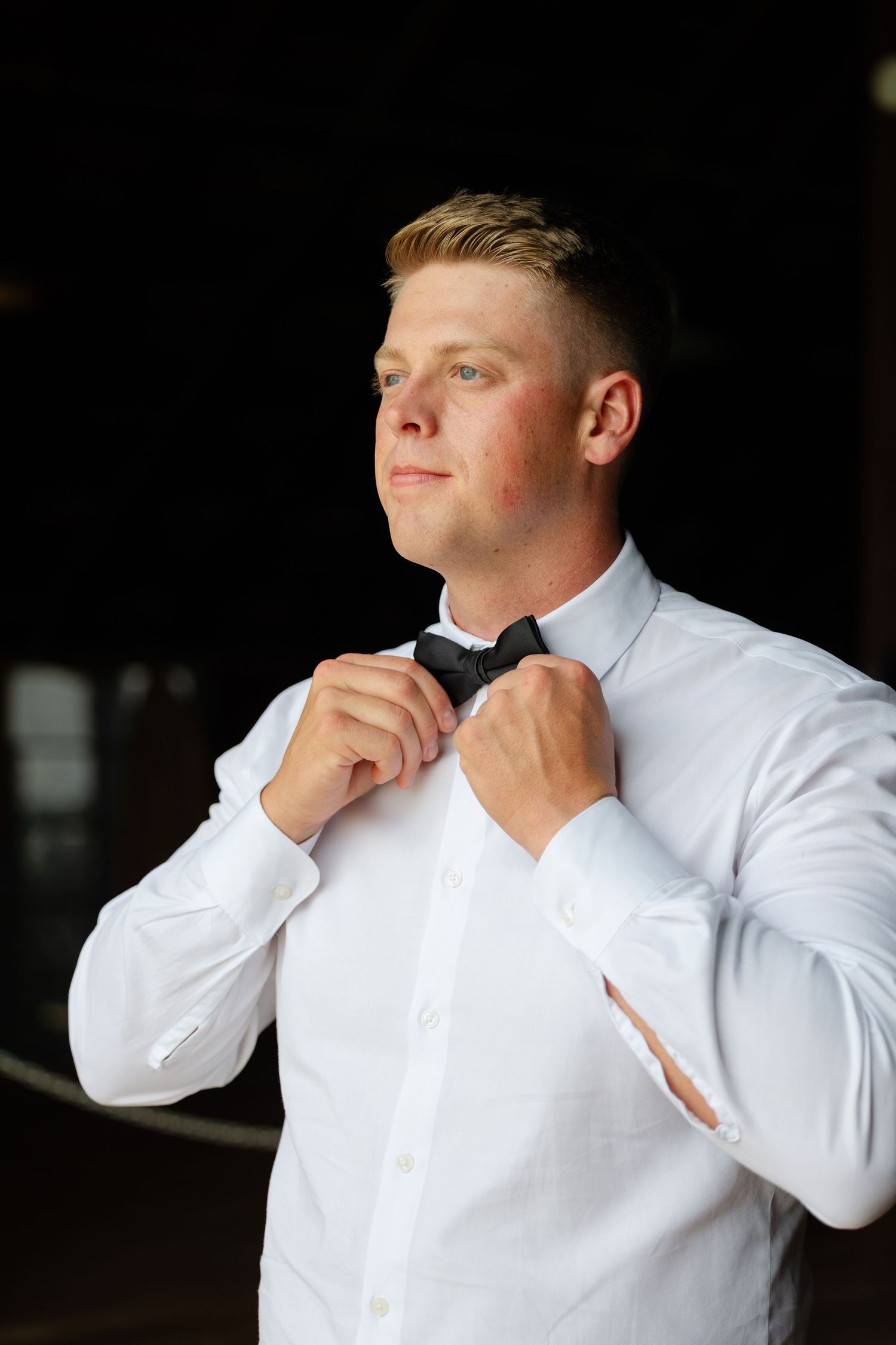 Person in white dress shirt adjusts collar and tie while looking away in dramatic lighting sequence.