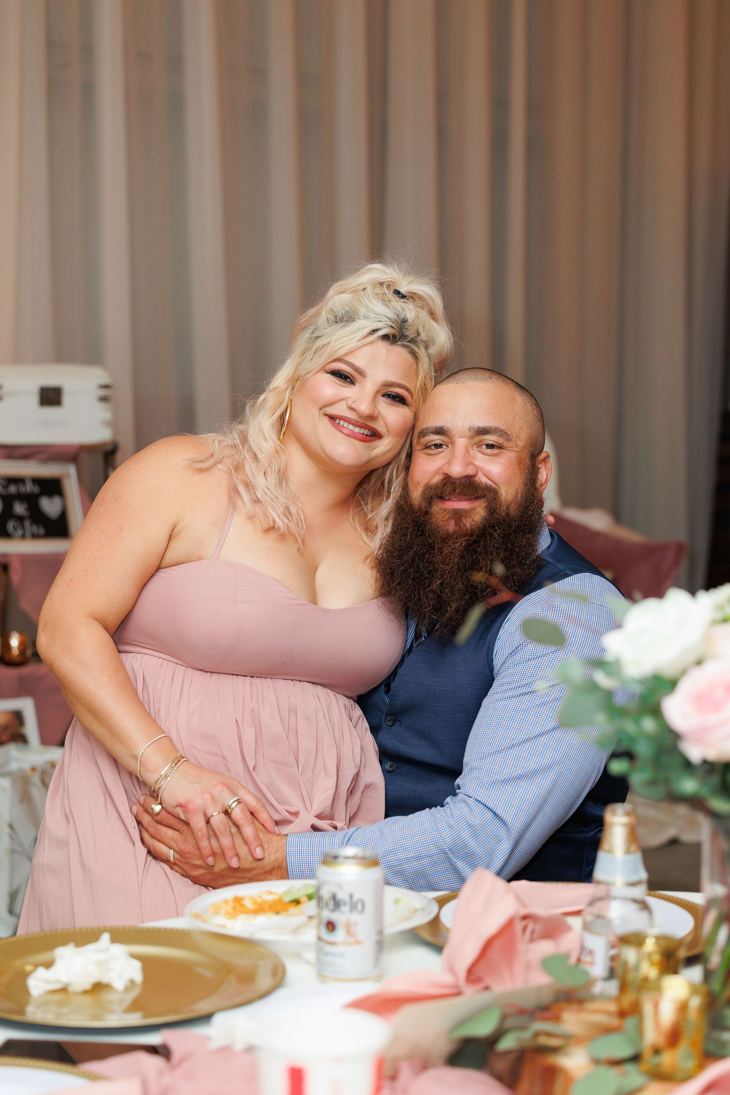 A couple shares an intimate moment at a dinner table decorated with pink flowers and place settings.