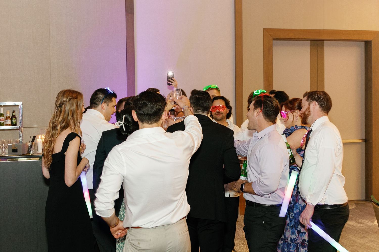 A group of people in formal attire dancing together in a reception hall during a social event.