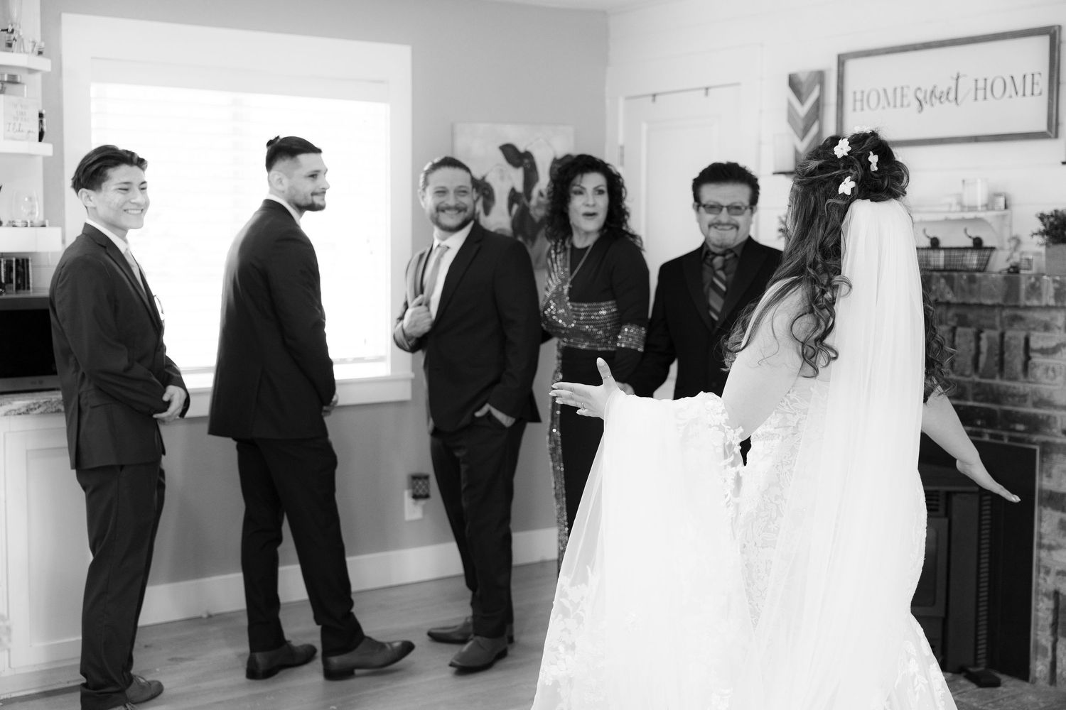 People wait in line along a white hallway wall with some wearing dark formal attire.