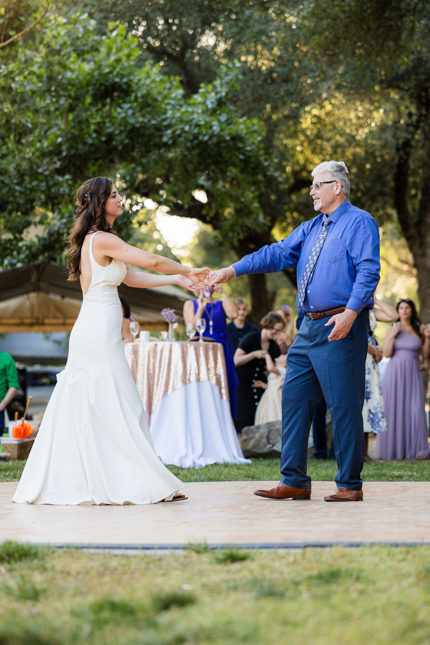 A couple shares a playful dance sequence at an outdoor wedding reception with bridesmaids in lavender dresses watching.