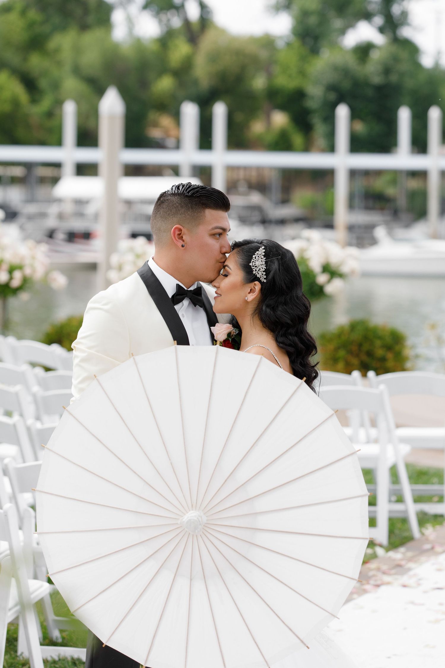 A romantic couple shares a kiss behind a white parasol at an outdoor wedding ceremony venue.