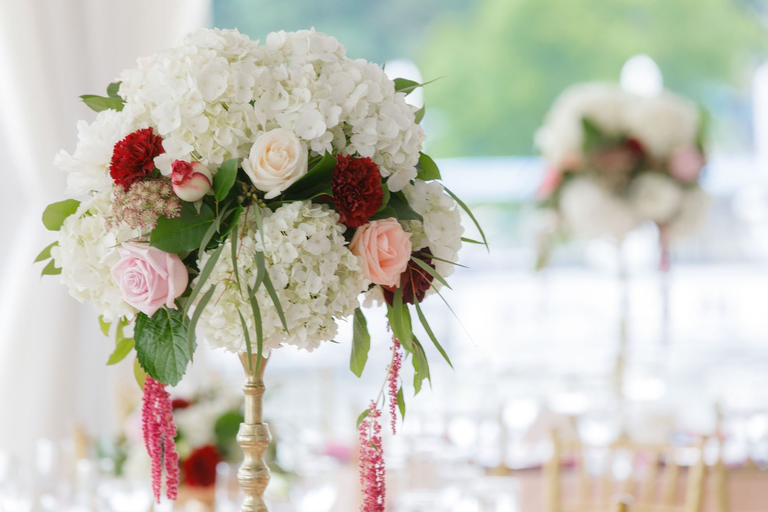 Elegant wedding reception tables decorated with tall floral centerpieces featuring red and pink roses with greenery.