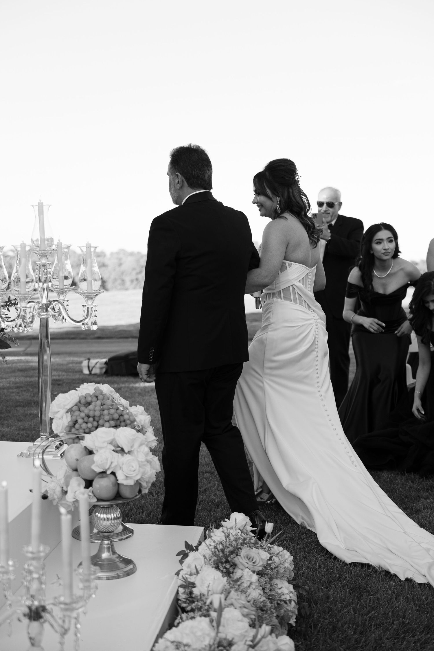 Elegant wedding reception details with crystal candelabras and white floral arrangements on outdoor tables at sunset.