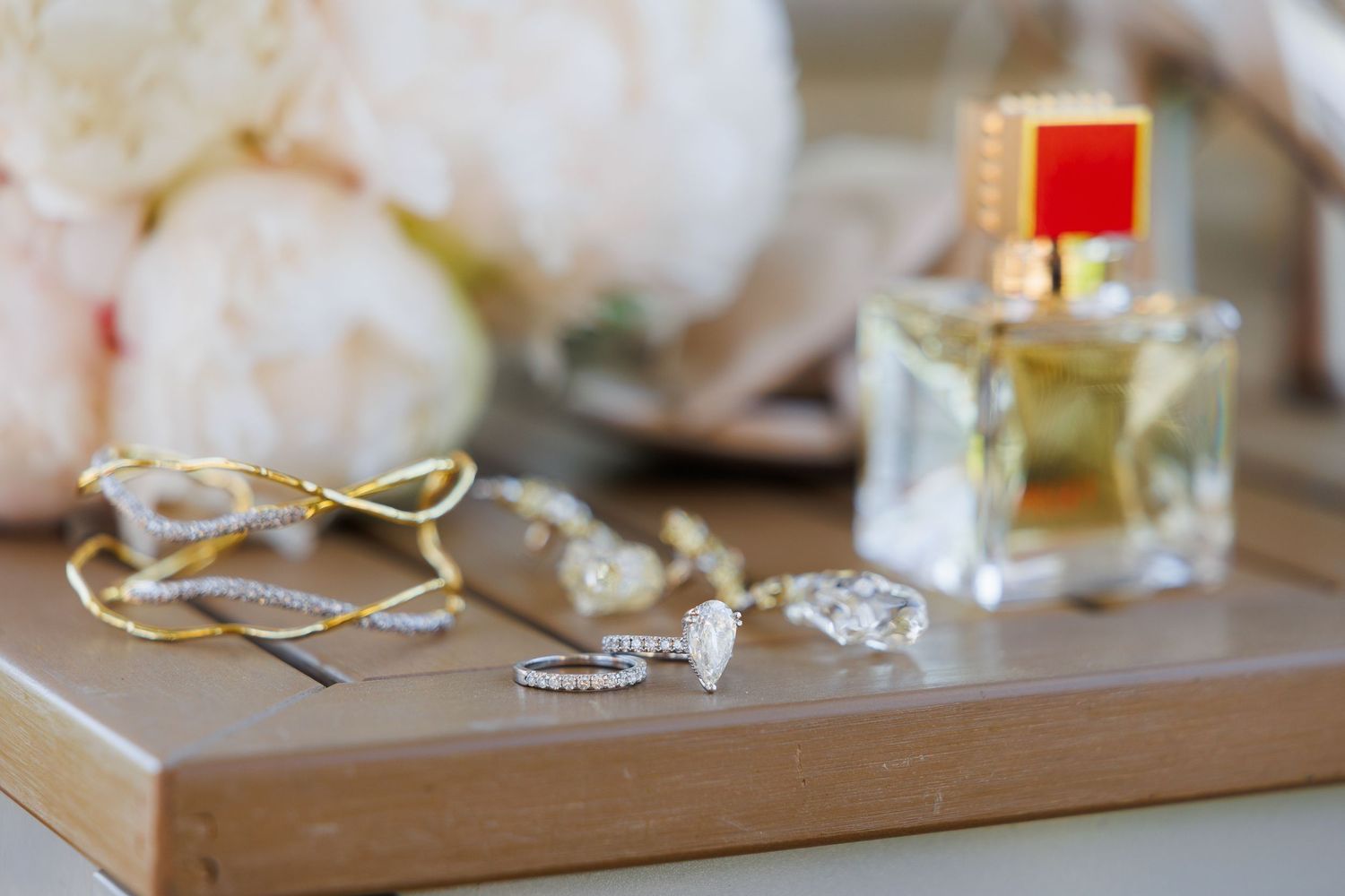 Elegant gold and silver jewelry pieces displayed on a wooden tray with delicate floral arrangements.