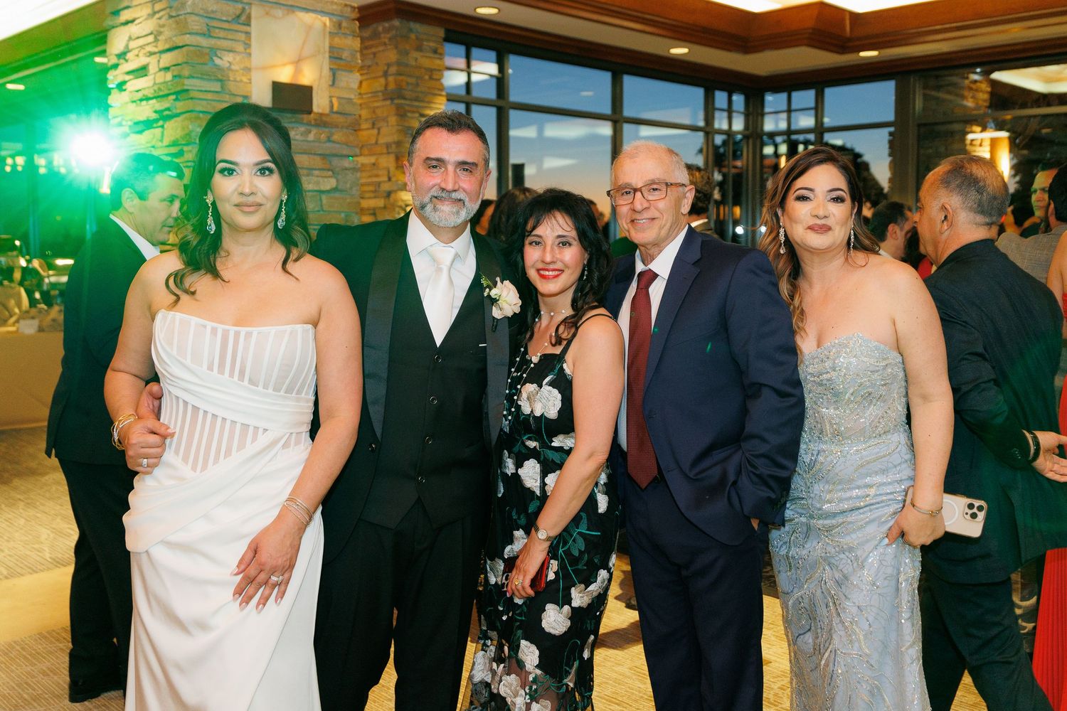 Group of people in formal attire at an elegant indoor event with stone walls and warm lighting.