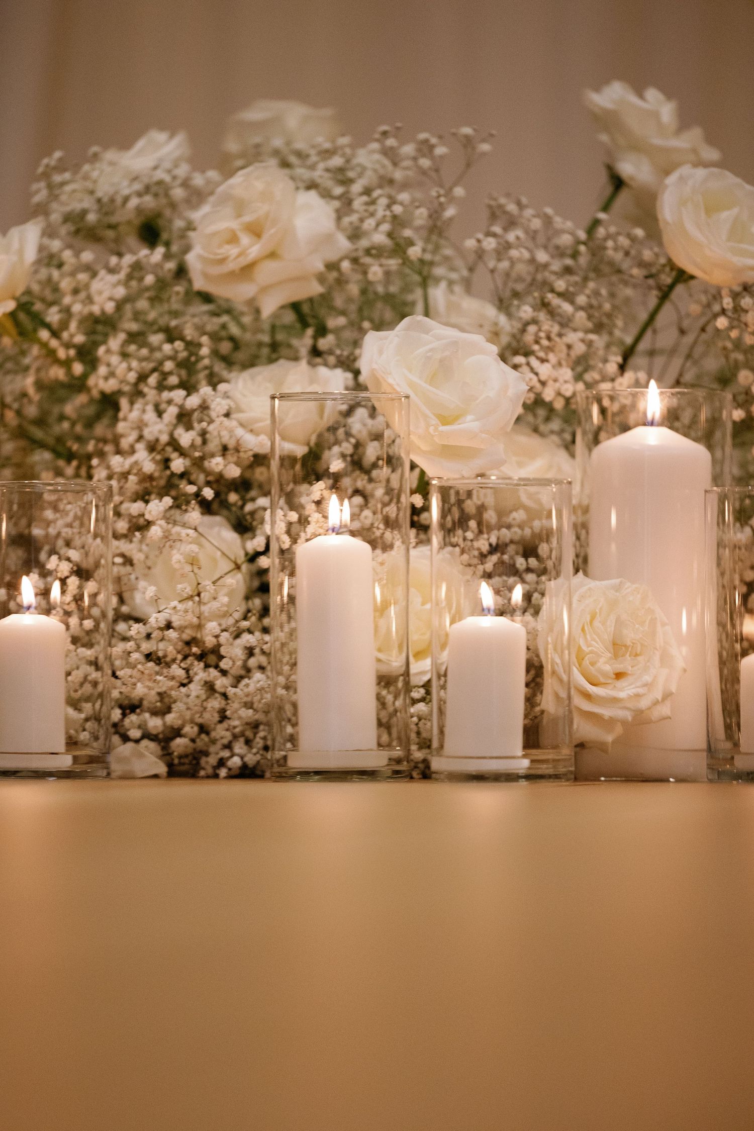 White pillar candles and delicate roses create an elegant wedding table centerpiece with soft romantic lighting.