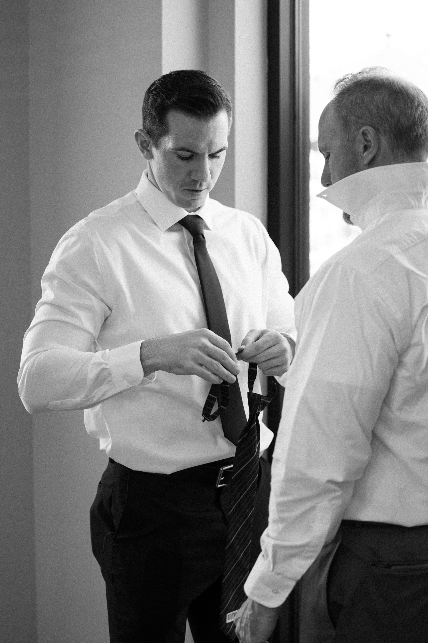 A sequence of black and white photos showing someone adjusting a necktie in progressive steps.