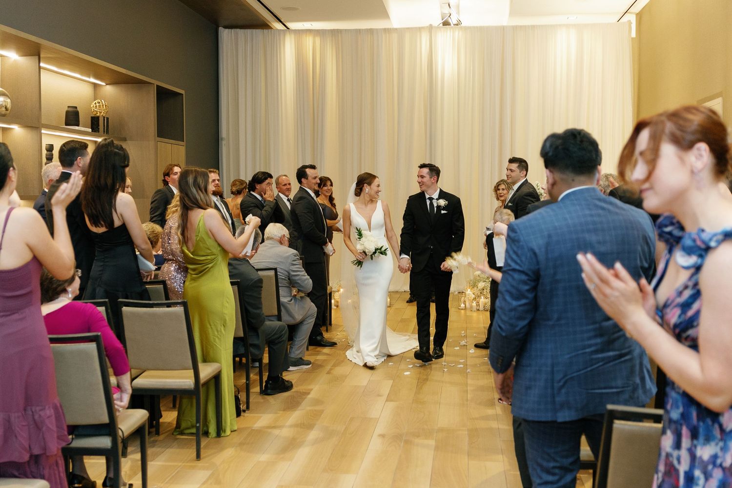 Wedding guests stand and applaud during a celebration in an elegant indoor venue with bright lighting.