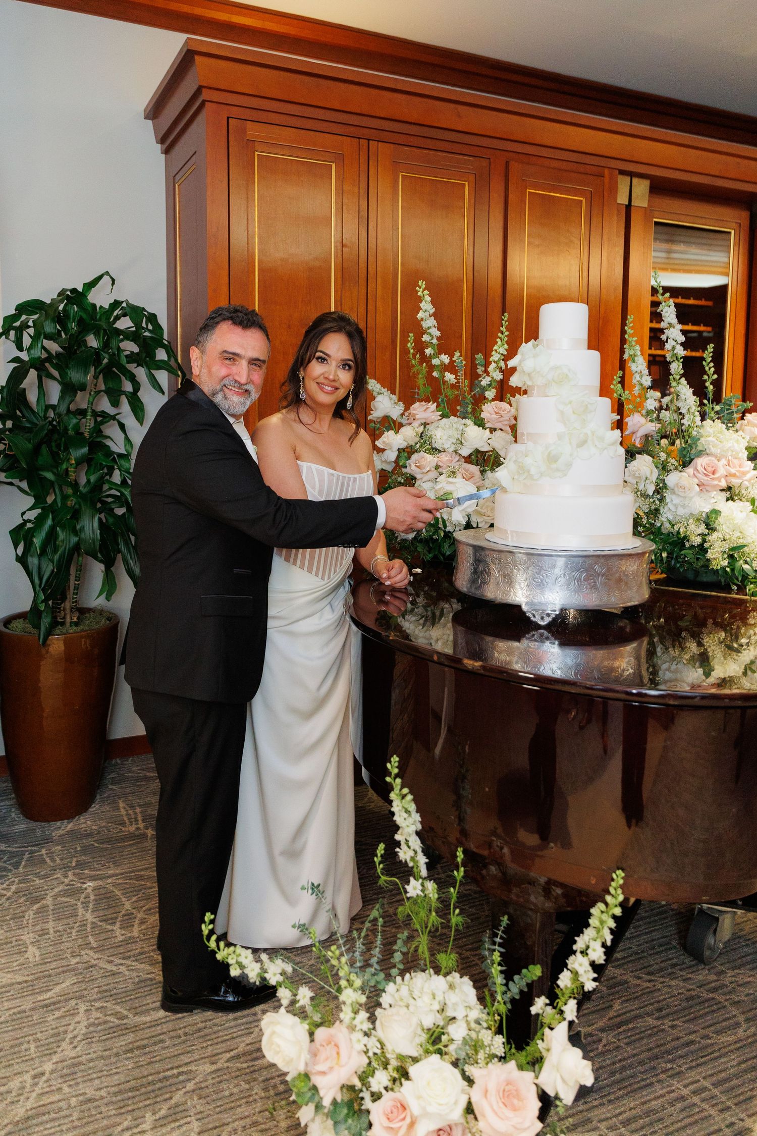 A beautiful white wedding cake adorned with fresh flowers sits on a wooden table surrounded by floral arrangements.