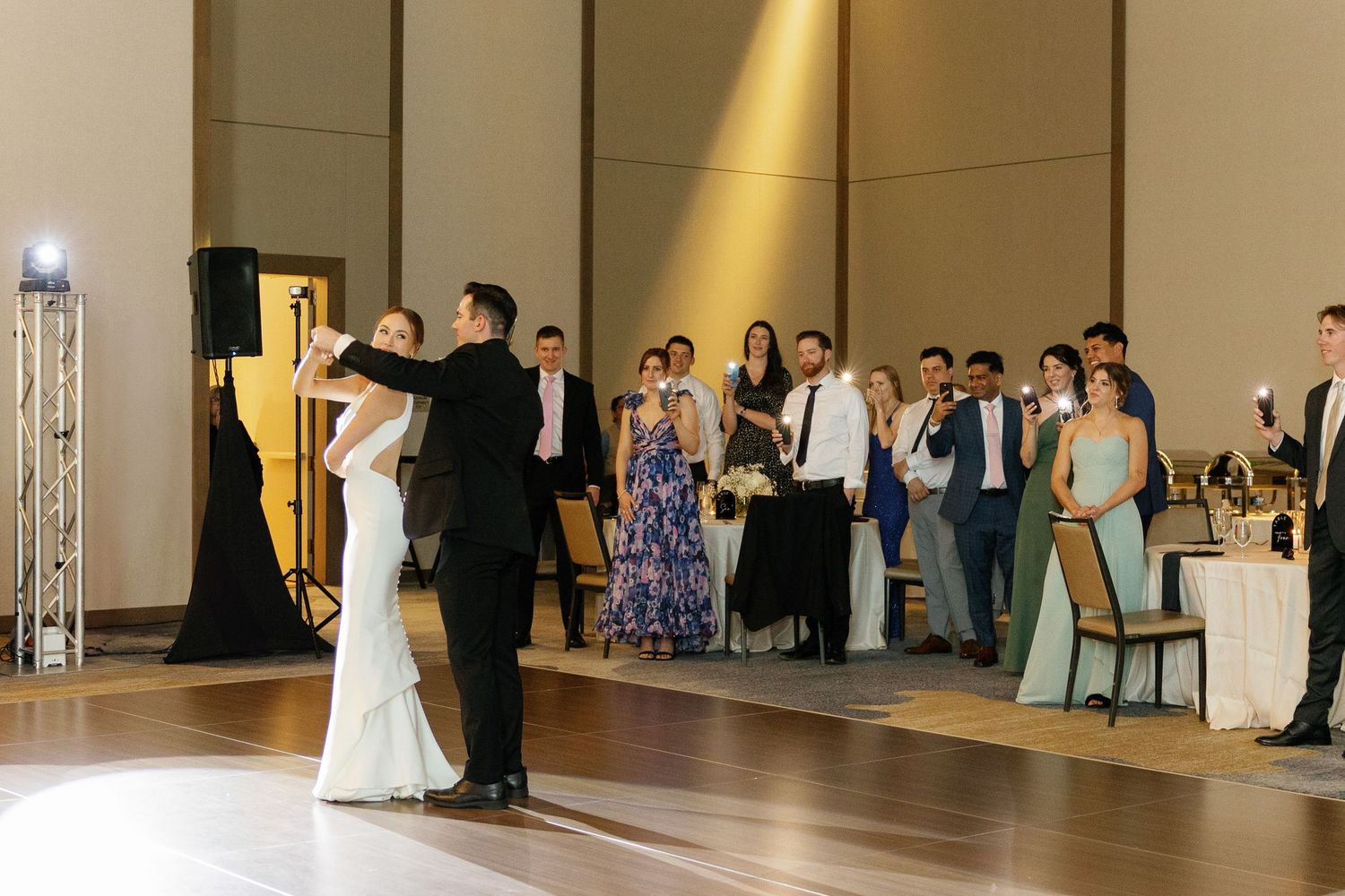 A panoramic view of a wedding reception in a spacious ballroom with guests dancing and mingling under warm lighting.