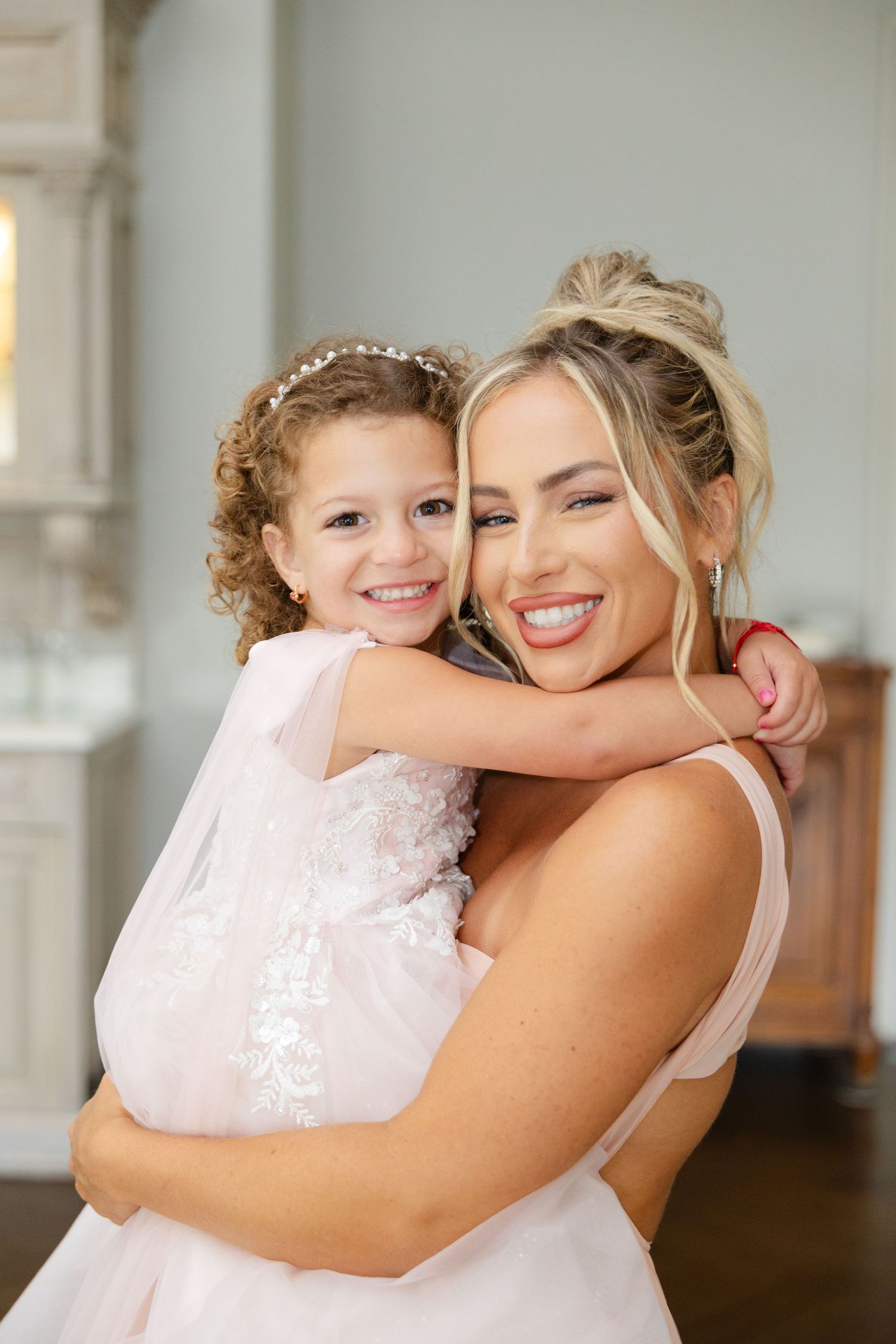 A heartwarming embrace between two people in light pink dresses with matching delicate hair accessories.